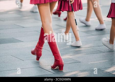Close up of majorette legs showcasing red boots and short skirts, marching confidently outdoors during a vibrant parade celebration Stock Photo