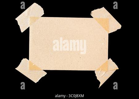rectangular piece of blank brown paper affixed with four masking tape isolated on black background Stock Photo
