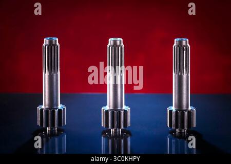 Three polished metal shafts stand on a dark surface, illuminated by a warm, reddish-brown gradient background. The shafts are identical in design, fea Stock Photo