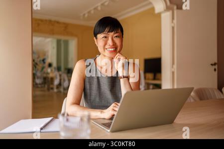 Portrait of smiling businesswoman browsing internet and sending emails over laptop at desk in office Stock Photo