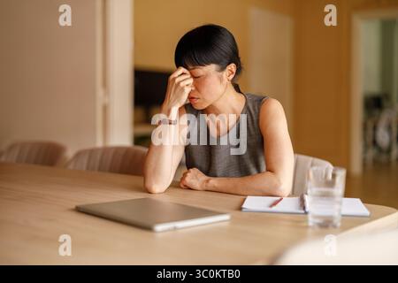 Overworked businesswoman with head in hands feeling stressed while working on deadlines at corporate office Stock Photo