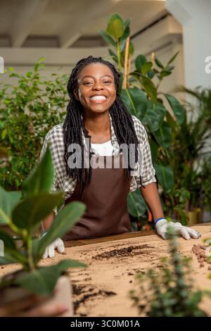 Cute african american woman in apron standing at the desk with plants Stock Photo