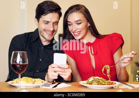 Smiling man and woman using mobile phone during dinner Stock Photo