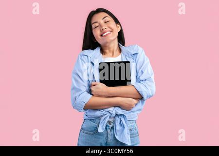 Excited asian woman hugging digital tablet at studio Stock Photo