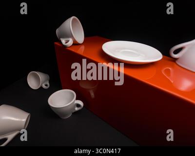 Several white ceramic cups and saucers are arranged on a brown wooden surface. Some cups are tipped over, creating a dynamic and slightly chaotic comp Stock Photo