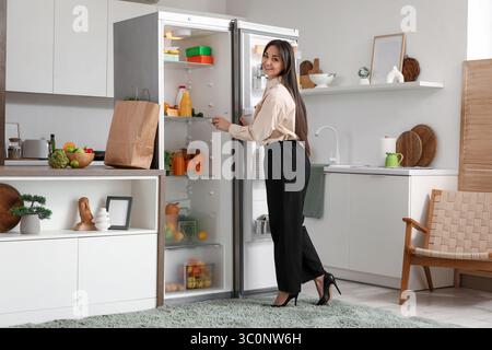 Beautiful businesswoman taking food from open fridge in kitchen Stock Photo