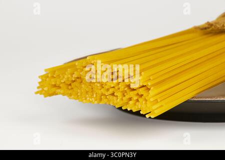 Raw spaghetti in a bundle tied with string on a white background with copy space, traditional Italian pasta. Stock Photo