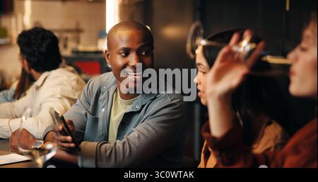 Happy, phone and friends in restaurant talking for bonding, social gathering and networking on weekend. Relax, bar and man with woman in conversation Stock Photo