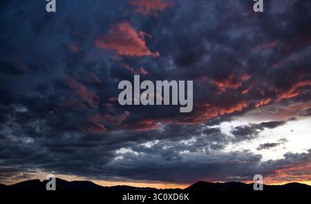 Colorful evening sky with dramatic clouds displaying beautiful orange, pink, and purple hues over a dark mountain silhouette. Stock Photo