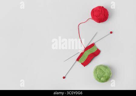 Red knitted wool on gray background with knitting needles for knitting warm clothes and hobbies needlework. Knitting a striped Christmas scarf with re Stock Photo