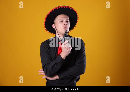 Man in black Flamenco hat with gun on yellow background Stock Photo