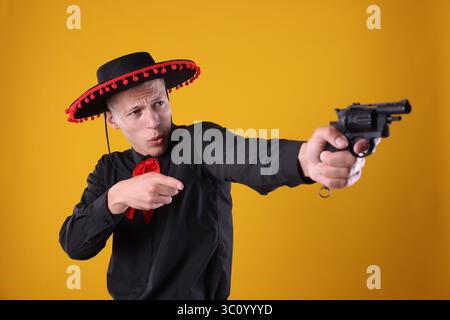 Man in black Flamenco hat with gun on yellow background Stock Photo