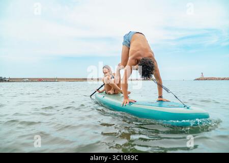 Young couple practicing acroyoga on a stand up paddle board in the sea Stock Photo