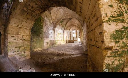 Ancient stone archways with moss-covered walls in a dimly lit corridor. Krak des Chevaliers castle, Syria Stock Photo
