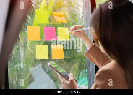 Young creative team use post it notes to share idea sticky note on glass wall. Working design planning and Brainstorming concept Stock Photo