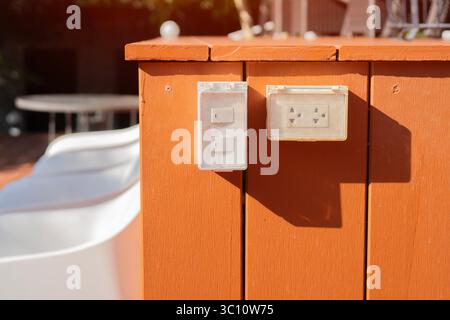 Outdoor white electrical outlet with cover on bright brown wooden wall. Selctive focus. Stock Photo