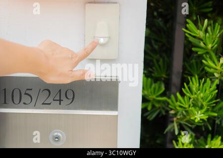 Woman hand is pressing the button on door bell in front of the house. Ring a doorbell concept. Stock Photo