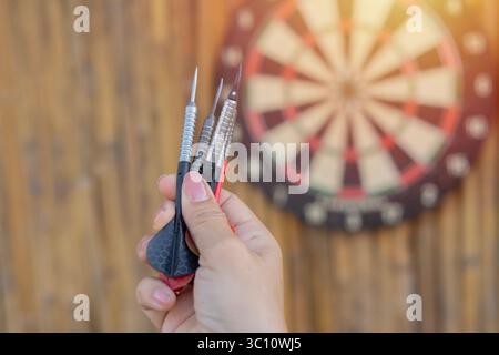 Close up shot black and red darts arrows in women hand over dartboard game standing outdoors on a sunny day. Selective focus. Stock Photo