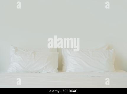Comfortable soft pillows on the bed. Close-up white bedding sheets and pillow on light wall room background. Copy space. Stock Photo