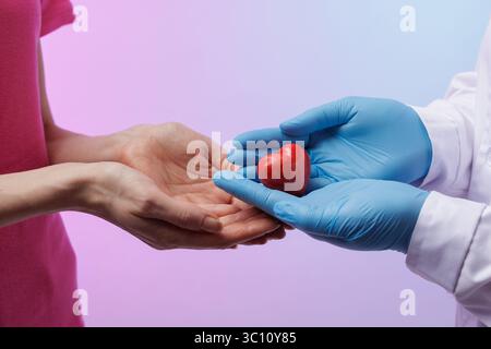 doctor's hands in gloves and woman holding red heart close up, modern medicine concept Stock Photo