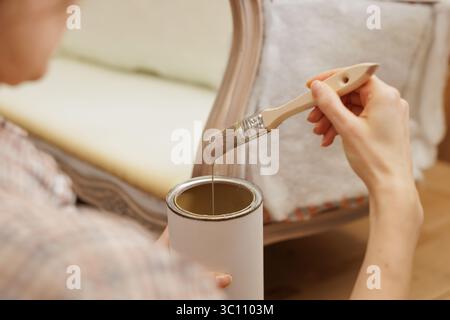 woman holding brush and can of paint and applying on old restored furniture, furniture repair Stock Photo