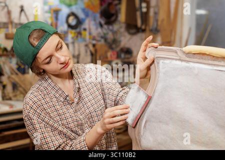 Woman working on upholstery fabric of furniture in workshop, restoration of old furniture, Stock Photo