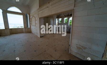 Abandoned building interior with arched windows and empty rooms, overlooking a distant landscape. The walls are worn, and the floor is tiled Stock Photo