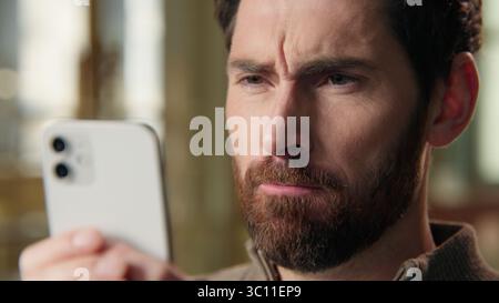 Close up annoyed stressed angry Caucasian businessman mad guy business man using mobile phone typing message texting smartphone online chatting gadget Stock Photo
