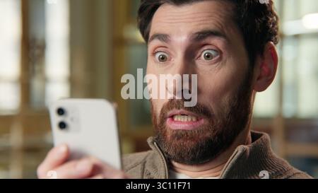 Close up shocked business man big eyes staring mobile phone screen shock wonder amazed stunned reaction message news in office afraid excited Stock Photo