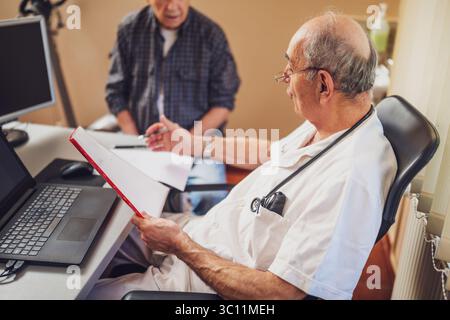 Elderly patient is having exam at cardiologist. Doctor is looking at his medical files. Stock Photo