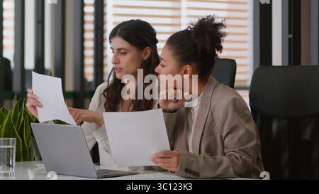 Multiethnic diverse girls ladies women business partners coworkers African American Caucasian female teamwork review documents using laptop analyze Stock Photo