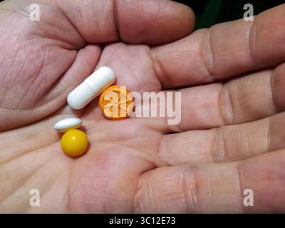 Different pills and vitamins in palm of male hand. Hand of man holds different pills. Medical concept, health. Close-up. Stock Photo