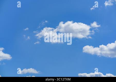 A vibrant blue sky filled with fluffy white clouds creates a serene atmosphere. The daylight enhances the beauty of the sky, inviting relaxation and c Stock Photo