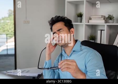Exhausted Office Worker Experiencing Headache from Intense Workload in Modern Workplace Setting Stock Photo