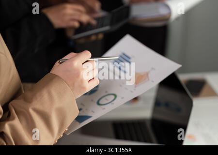 Businessman Analyzing Stock Graphs on Laptop and Paper Charts in Modern Office Setting for Financial and Investment Insights Stock Photo