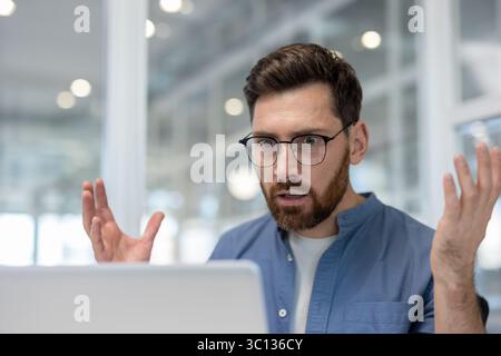 A man with glasses is surprised by something he sees on his laptop. He has his hands up in disbelief. Stock Photo
