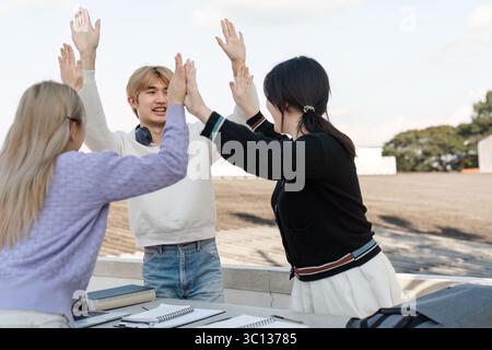 Asian College Students Celebrating Academic Success with High Fives and Smiles Outdoors on Campus Stock Photo