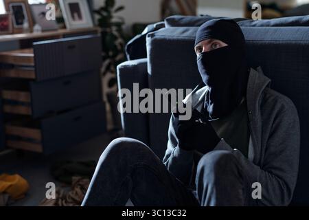 Man Wearing Mask Holding Gun Sitting Indoors Stock Photo