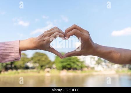 Affectionate heart gesture between two hands outdoor park human connection natural setting close-up perspective love concept Stock Photo