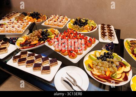 Wide variety of desserts and fruits served on a catering table. Includes eclairs, fruit tarts, chocolate cakes, and fresh fruit. Stock Photo