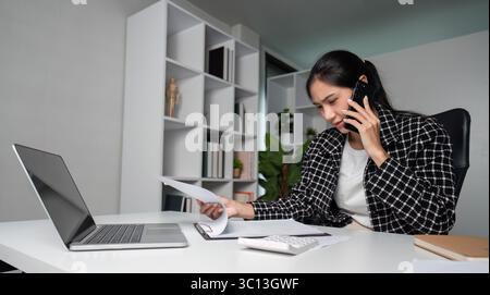 Dedicated Businesswoman Working Overtime in Modern Office with Laptop, Phone, and Documents for Professional Success and Productivity Stock Photo