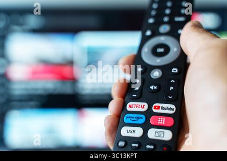 Tbilisi, Georgia - July 2, 2025: Close-up photo of a smart TV remote control featuring dedicated buttons for popular streaming platforms like Netflix, YouTube, and Amazon Prime, with a television screen blurred in the background. Represents modern digital media consumption, subscription-based services, and on-demand entertainment. Ideal for tech, streaming, binge-watching, or media lifestyle content. Stock Photo