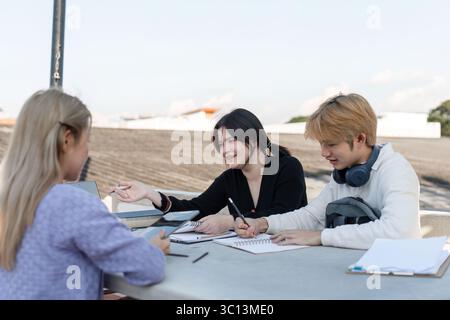 Diverse Group of Students Engaged in Online Learning Outdoors with Laptops and Notebooks Stock Photo