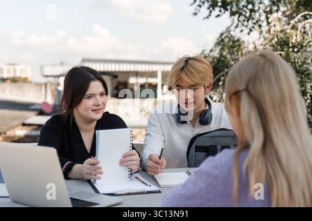 Diverse Group of Young Students Collaborating and Studying Together Outdoors with Laptops and Notebooks in a Modern Educational Setting Stock Photo