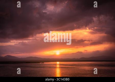 View of a radiant sunset paints the sky with fiery hues over a tranquil lake, casting a golden glow on the water's surface, Balykchy, Kyrgyzstan. Stock Photo