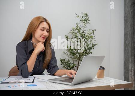 Professional Businesswoman Analyzing Financial Graphs on Laptop in Modern Office Setting with Coffee Stock Photo