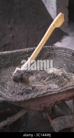 A wheelbarrow filled with wet cement and a shovel in the middle of a building project, illustrating the labor and dedication behind every construction Stock Photo