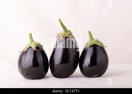 Three black eggplants are sitting on a white background. The eggplants are all different sizes and are arranged in a row Stock Photo