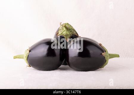 Three black eggplants are sitting on a white background. The eggplants are all different sizes and are arranged in a row Stock Photo