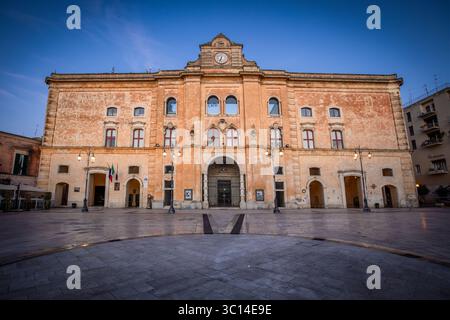 View of a grand, sun-kissed baroque structure stands proudly against the soft blue sky, its ornate facade casting long shadows on the quiet plaza, Sassi di Matera, Basilicata, Italy. Stock Photo